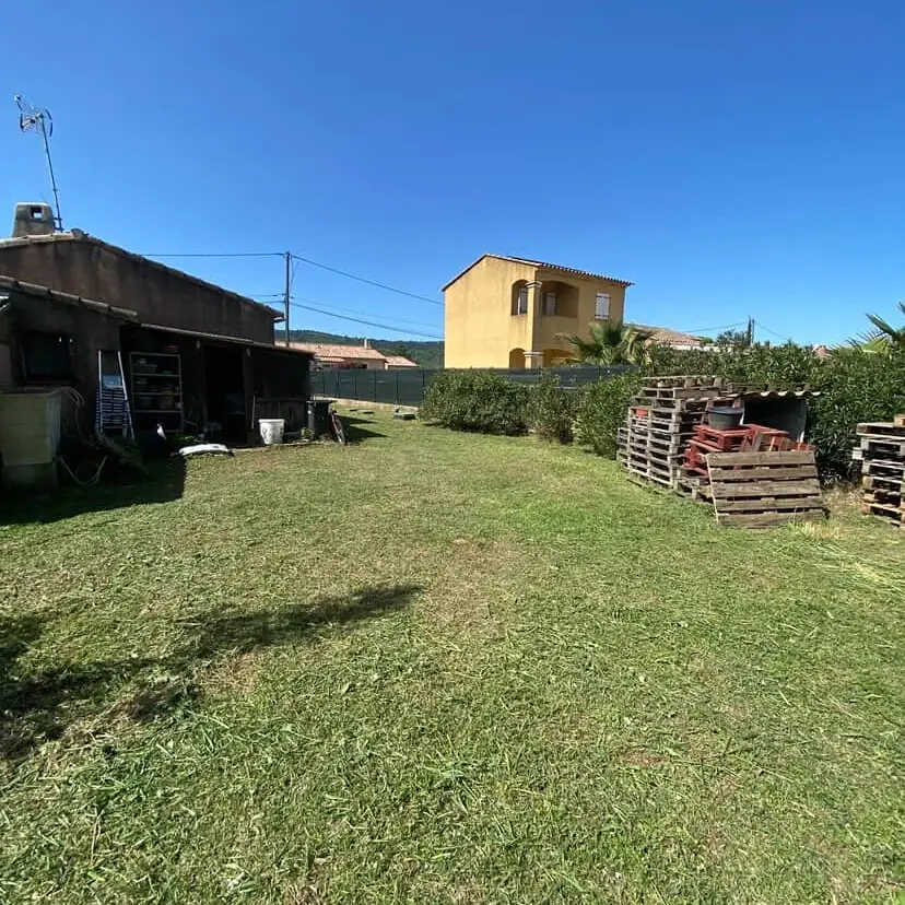 Pelouse de campagne tondue devant une remise, maison ocre en fond